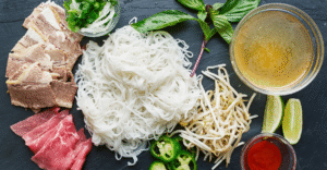 Pho vs. Ramen: Which One’s Right for You? 2 Flat-lay of pho ingredients: noodles, beef, herbs, broth, and garnishes—fresh and balanced.)