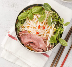 How Do You Make Pho Broth? The Secret Behind Authentic Flavor 1 Top-down view of Vietnamese pho with clear broth, rice noodles and aromatic herbs.